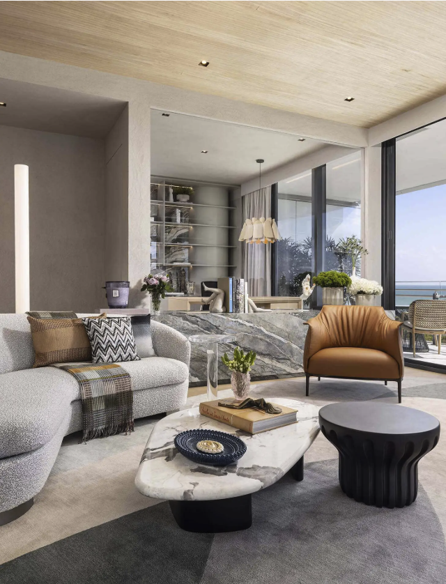 Oceanfront living room in a Miami Beach apartment featuring a boucle sofa, sculptural marble coffee table, leather accent chair, and seamless indoor-outdoor flow with ocean views.