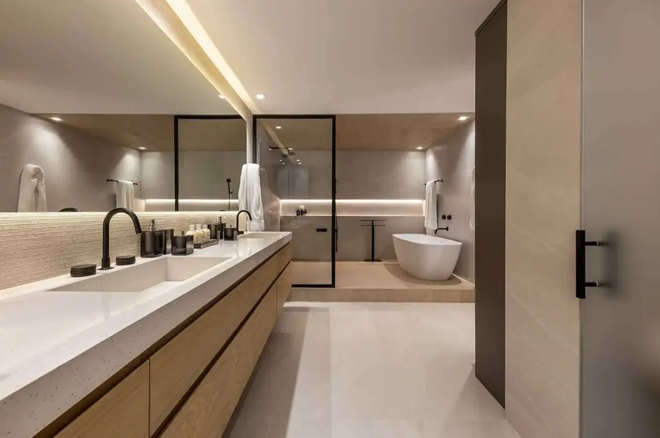 Modern minimalist bathroom featuring a double vanity with black fixtures, large backlit mirror, glass-enclosed shower, and freestanding tub.