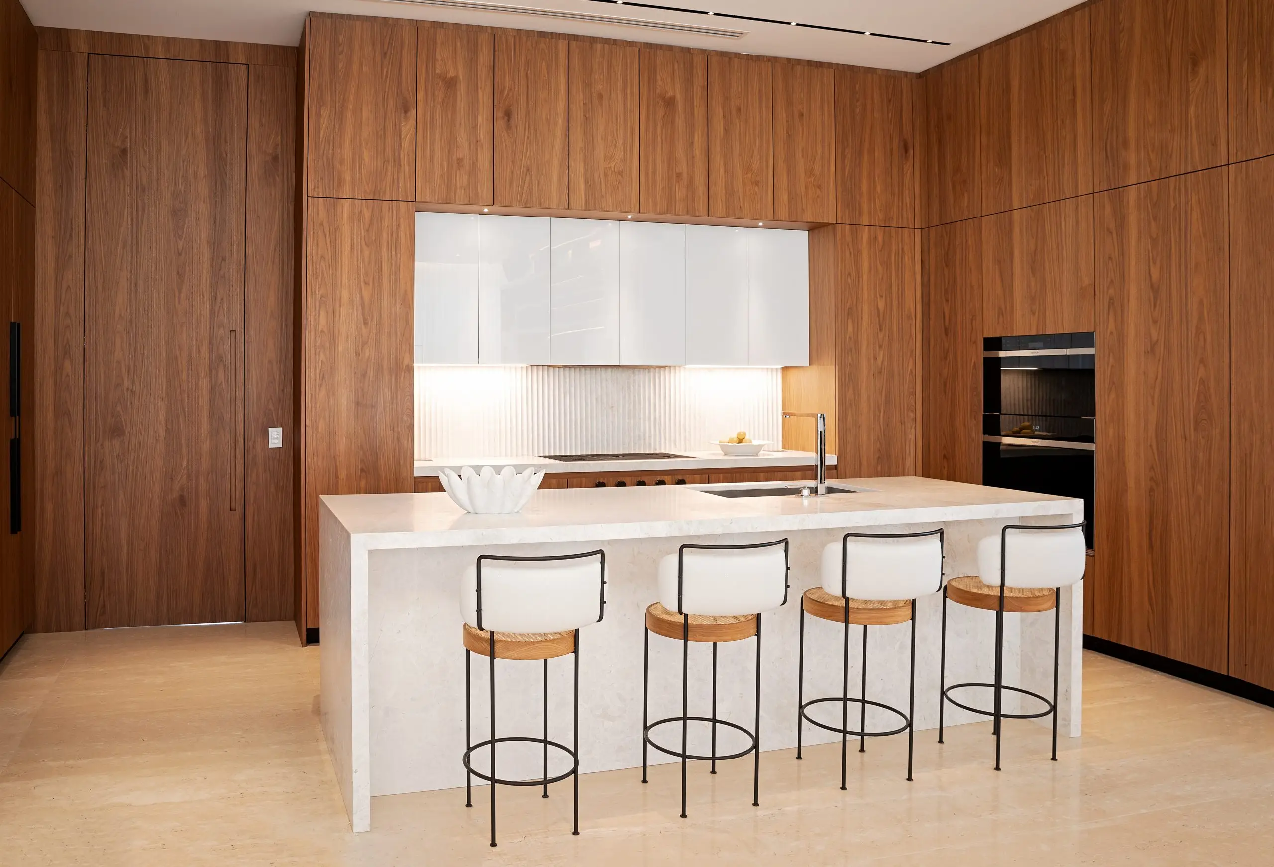 Minimalist luxury kitchen in a Venetian Island home featuring a marble island, wood-paneled walls, and modern bar seating