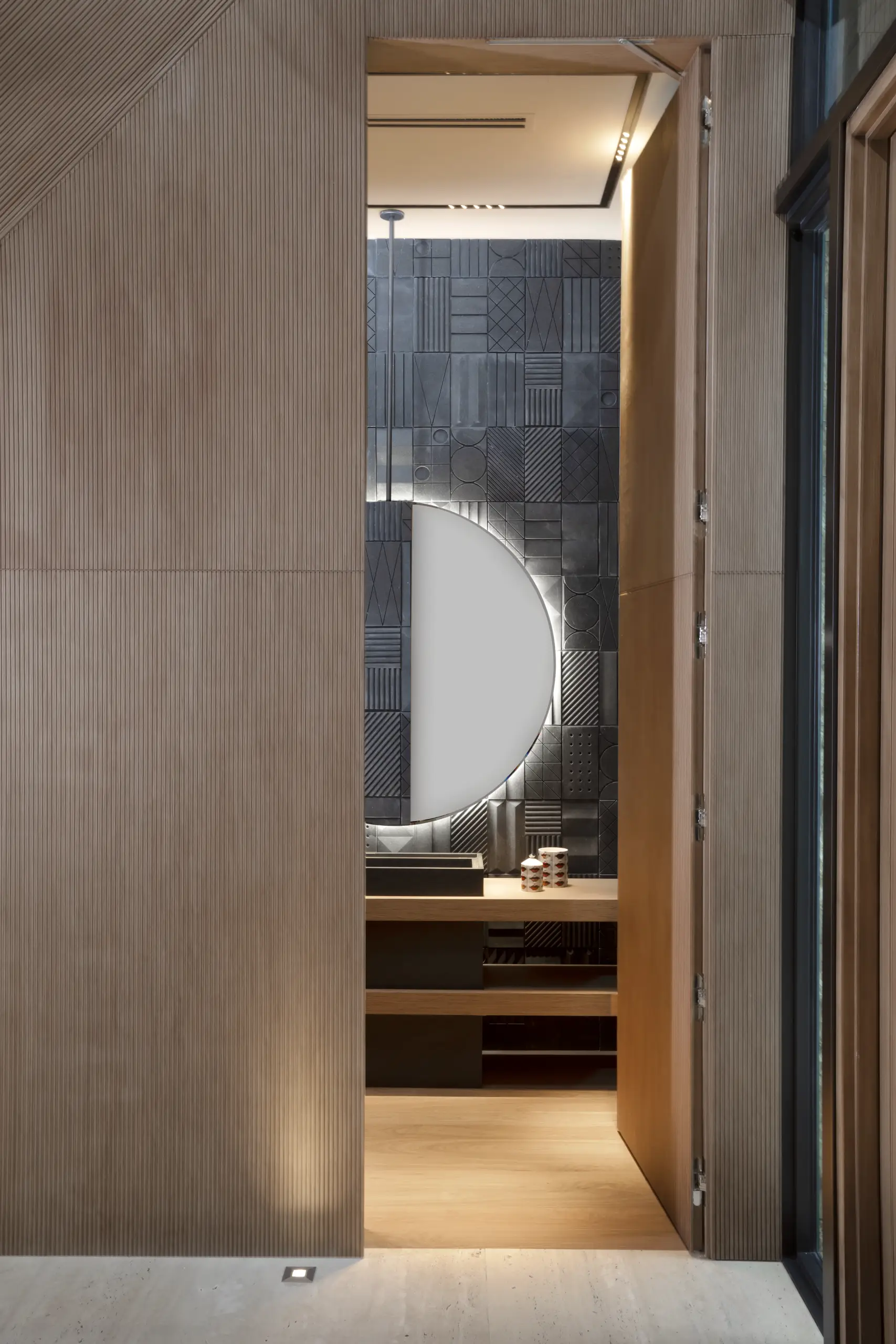 Sculptural half-moon mirror with backlighting and geometric black tile wall in a Venetian Island luxury home by Luciana Fragali