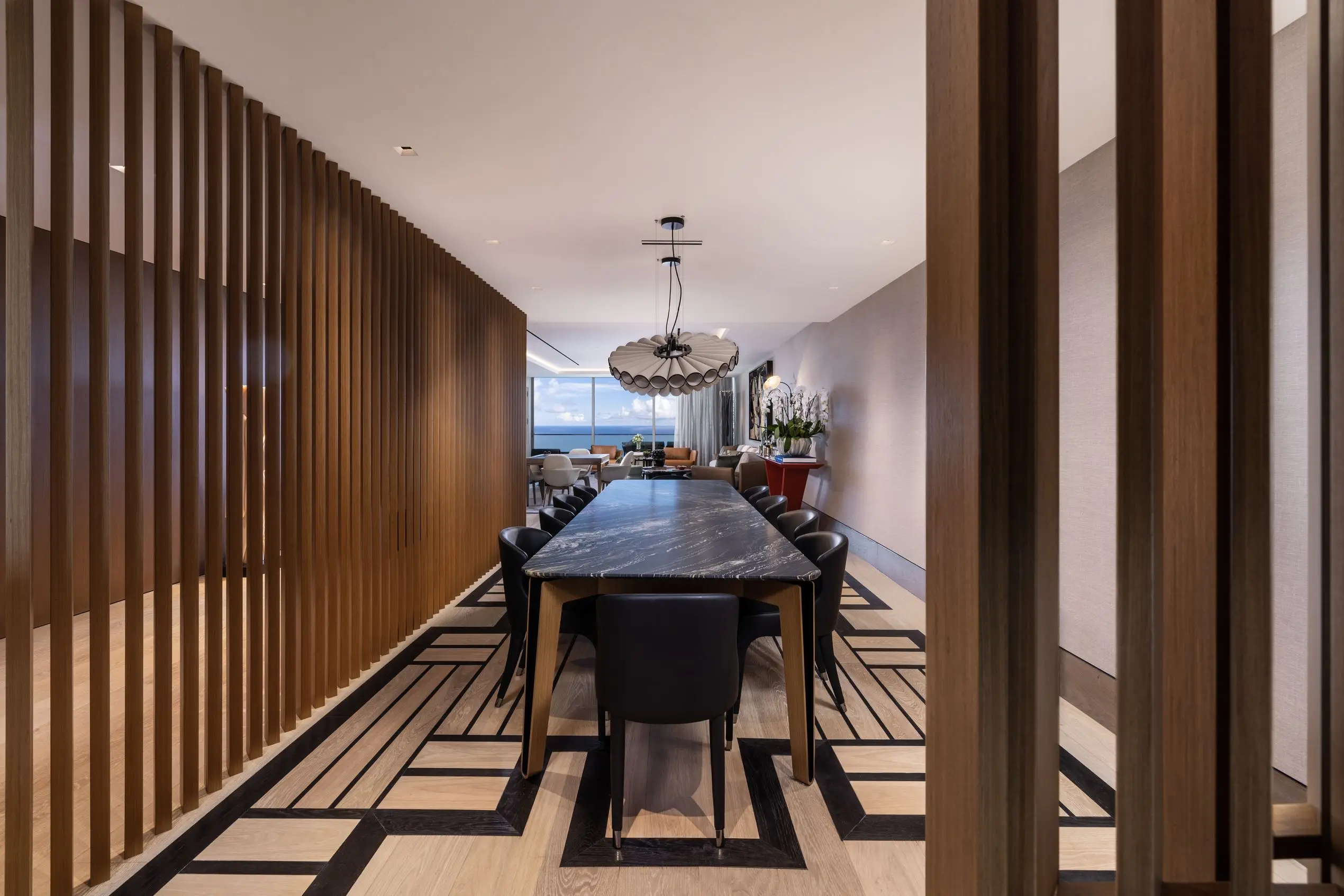 Contemporary dining area at Oceana Bal Harbour with black marble table, sculptural lighting, geometric flooring, and slatted wood partitions.