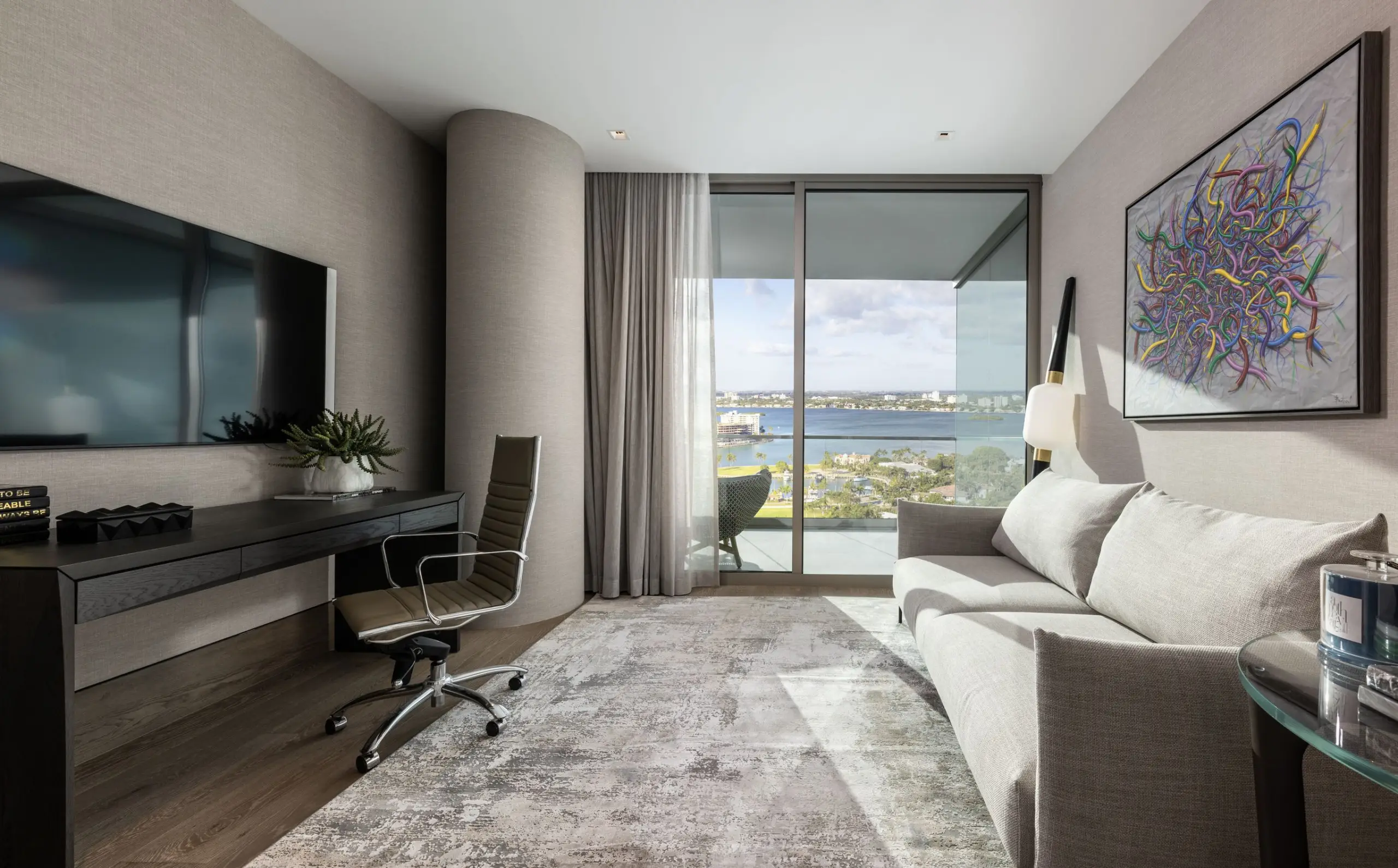Minimalist home office at Oceana Bal Harbour featuring built-in desk, modern swivel chair, abstract artwork, and floor-to-ceiling ocean views.