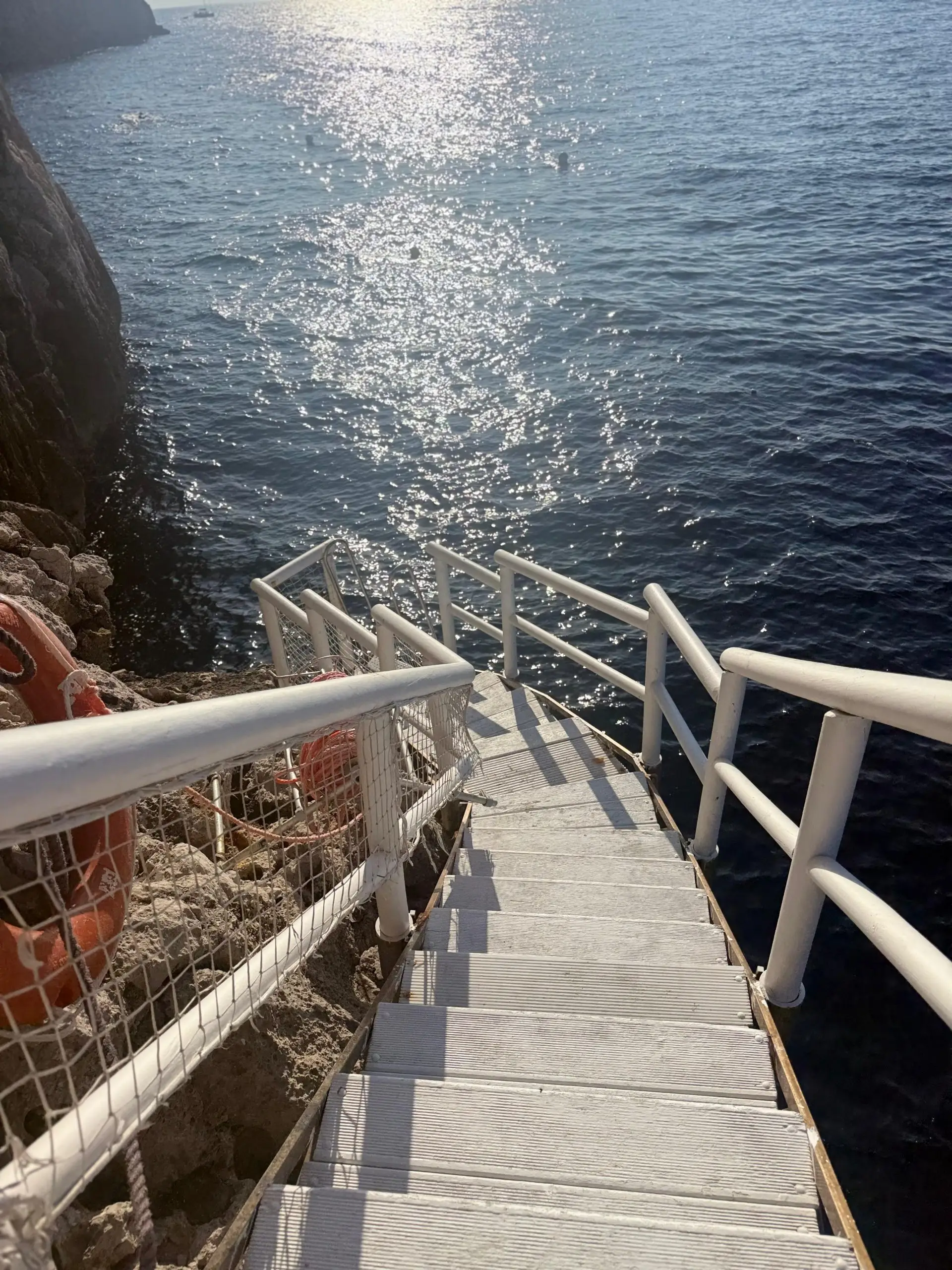 An example of visual tension in design, where modern white stairs are set against a timeworn, rocky cliff, creating an inviting path down to the glittering sea.