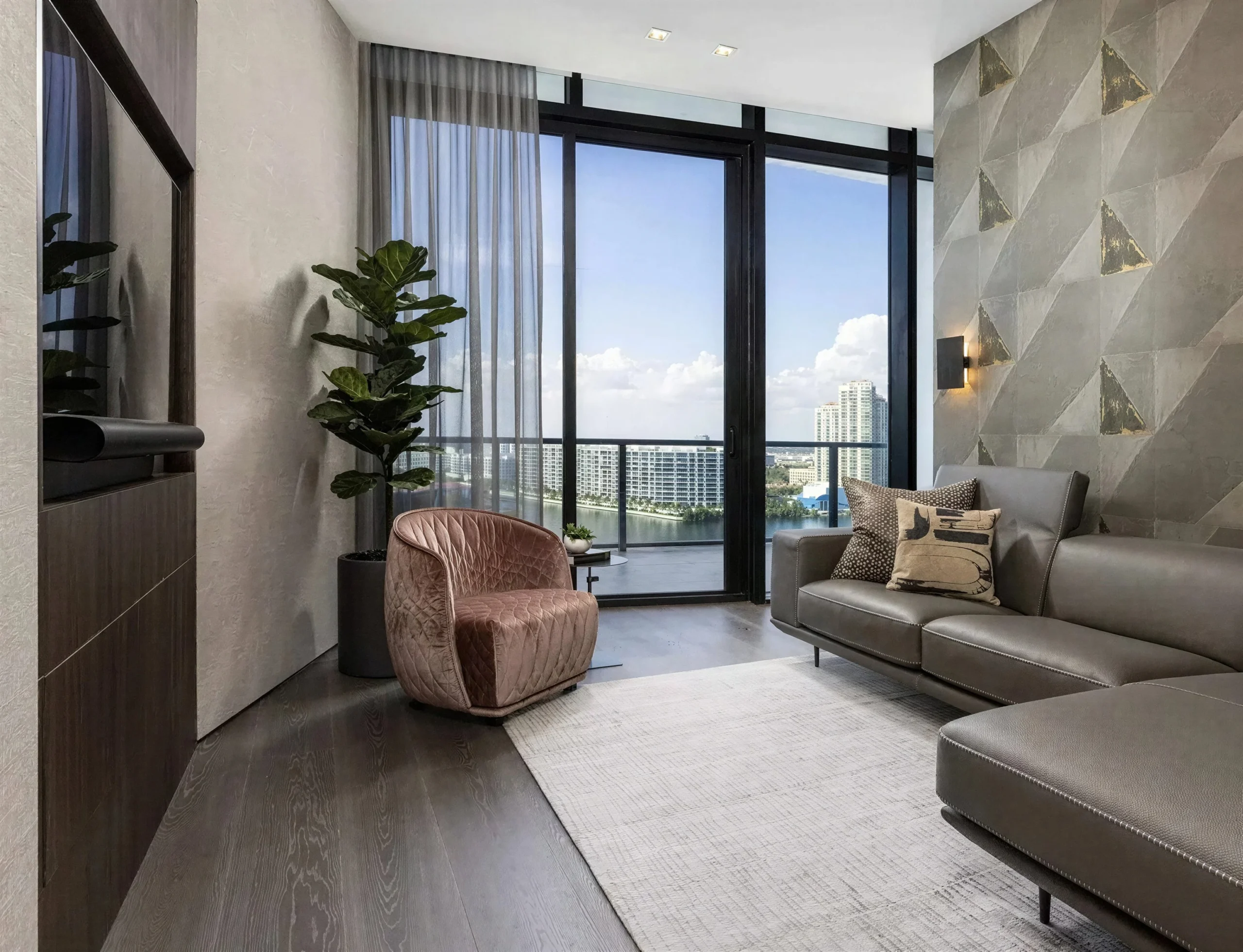 Luxury condo living room with gray leather sectional, pink velvet chair and floor-to-ceiling waterfront view